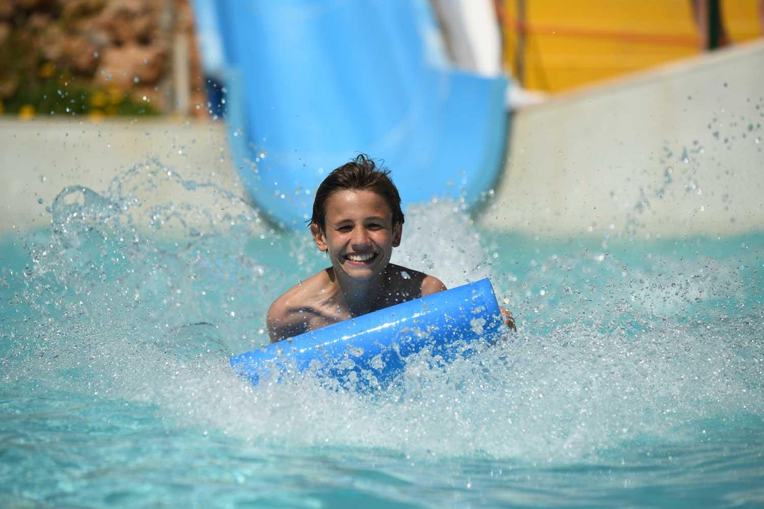 Criança sorridente a chegar à piscina no final de um escorrega
