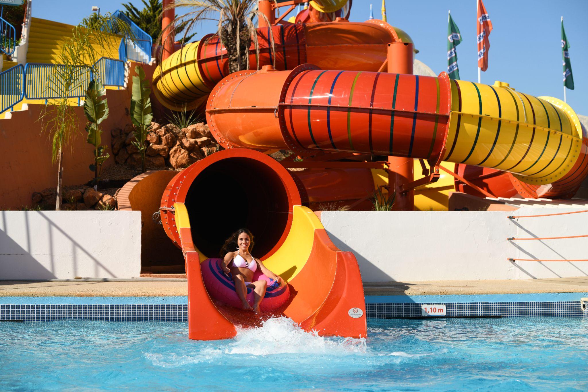 Visitante a sair de um escorrega laranja e amarelo para a piscina no Slide & Splash